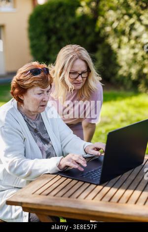 Elderly woman using laptop outdoors. Senior mother learning modern technology and digital skills from her adult daughter Stock Photo