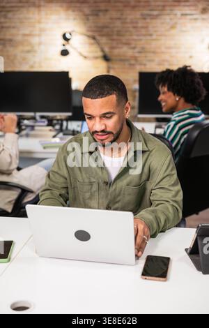 Focused young man working on laptop in busy office Stock Photo