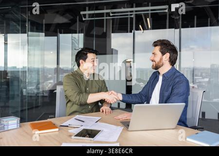Two diverse businessmen smiling and shaking hands, finalizing an agreement after a productive meeting in a modern office, representing partnership, success, and professional collaboration Stock Photo