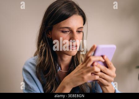 Focused young woman reading smartphone message with serious expression at home. Mobile communication, notification, concern and modern digital lifesty Stock Photo