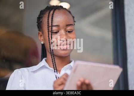 Young Black woman using tablet with stylus and smiling softly on stairs. Digital planning, note taking, online study, remote work, mobile productivity Stock Photo