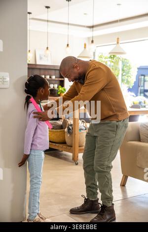African American father and child smiling, measuring height using bright pink ruler at home Stock Photo