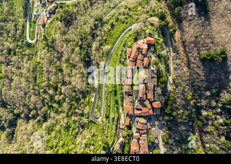 Aerial view of the small village of Trappola with its terracotta rooftops surrounded by dense green forests and winding mountain roads in Trappola, Tu Stock Photo