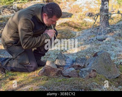 Man blowing to start campfire in forest during bushcraft Stock Photo