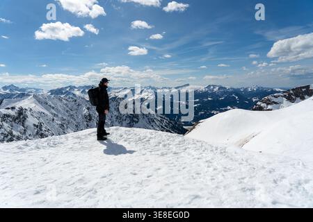 Hiker standing on snowy mountain ridge under dramatic clouds Stock Photo