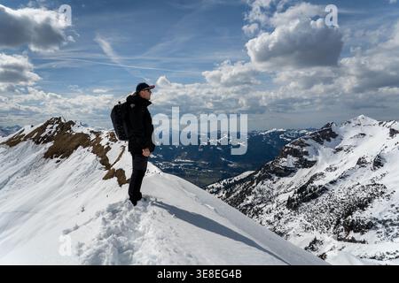 Hiker standing on snowy mountain ridge under dramatic clouds Stock Photo