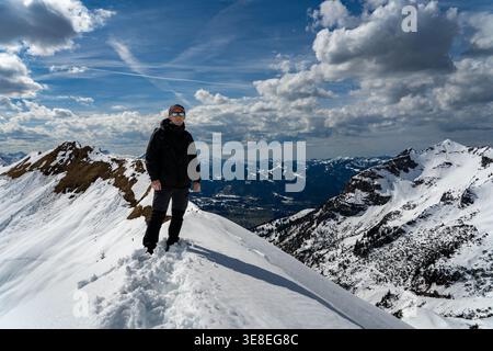 Hiker standing on snowy mountain ridge under dramatic clouds Stock Photo