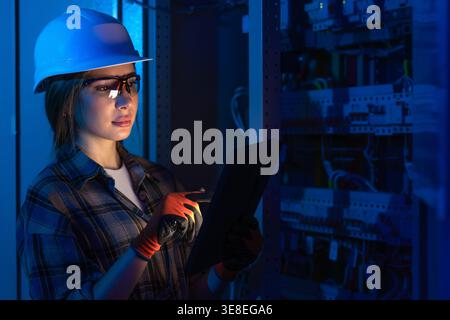 Female electrician inspecting electrical system using tablet device. Engineering diagnostics. Stock Photo