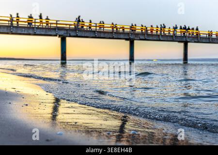 Sunset over sea pier with people silhouettes. Golden hour on the baltic beach landscape. Stock Photo