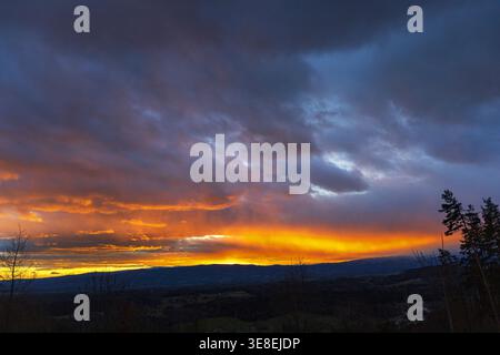 Beautiful sunset with glowing horizon and dramatic clouds over landscape. Stock Photo