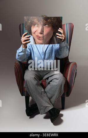 Young man sitting in armchair holding notebook covering face minimal studio portrait. Stock Photo