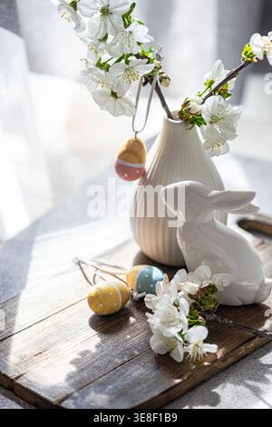 Close-up of a Spring table setting with a vase of cherry blossoms with assorted Easter ornaments on a wooden chopping board Stock Photo