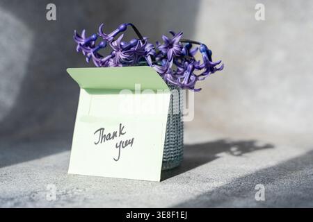 Thank you note in front of a vase of blue hyacinths on a table in sunlight Stock Photo
