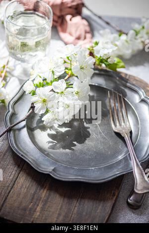Close-up of a rustic spring place setting with cherry blossoms on a pewter plate and a glass of water Stock Photo