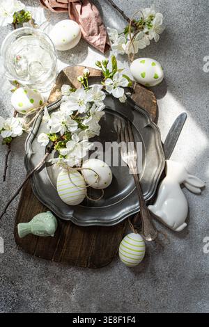 Overhead view of a rustic spring place setting with cherry blossoms on a pewter plate, assorted Easter decorations and a glass of water on a table Stock Photo