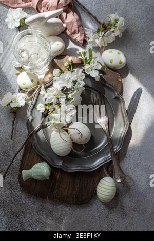 Overhead view of a rustic spring place setting with cherry blossoms on a pewter plate, assorted Easter decorations and a glass of water on a table Stock Photo