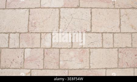 High-resolution image of a light-colored marble brick wall featuring subtle pink and gray veining. The textured orange stone brick surface is arranged Stock Photo