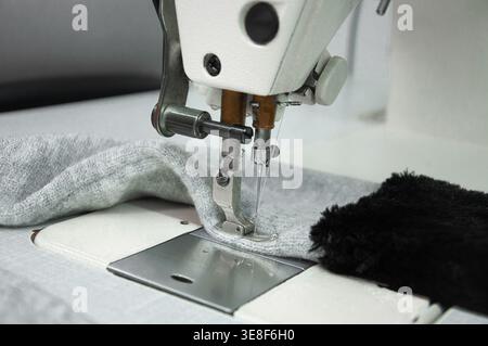 Close-up view of a sewing machine stitching fabric, focusing on the needle and presser foot during garment production, highlighting textile craftsmans Stock Photo