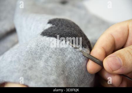 Close-up of a person repairing knitted fabric using a latch hook tool, highlighting textile mending techniques and sustainable clothing care practices Stock Photo