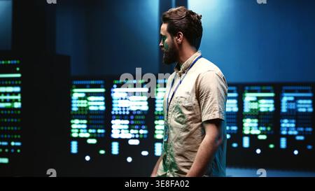 Engineer walking in server room housing advanced data storage infrastructure storing massive datasets, supporting critical workloads requiring IT equipment to run at high power densities Stock Photo