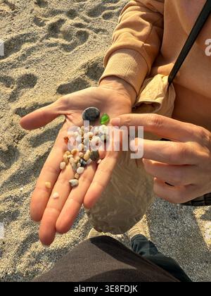 Hand collecting small pebbles and sea glass on sandy beach on a sunny day. Mobile photo Stock Photo