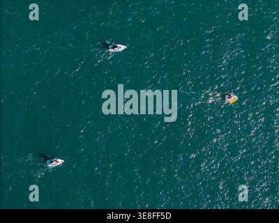 Aerial view of three small motorboats cruising across the sparkling turquoise sea with sunlight reflecting on the water surface. Stock Photo
