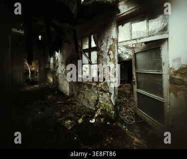 Abandoned corridor with broken windows and crumbling walls inside ruin. Stock Photo