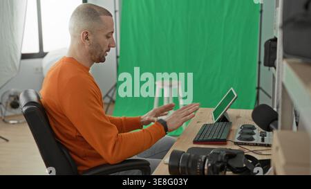 Man photographer pointing at tablet and gesturing with hands at desk in studio, green screen and camera visible; concentration creativity. Stock Photo