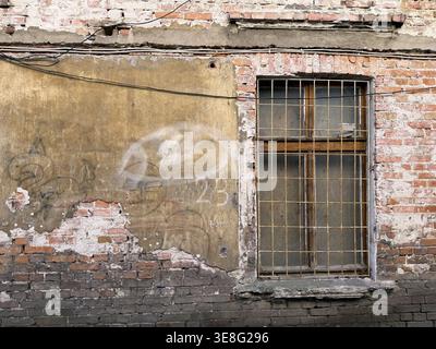 Old barred damaged window of brick building Stock Photo