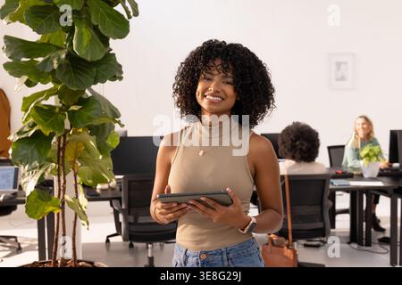 Tablet is displaying dashboard and glowing on desk in modern open-plan office with plant Stock Photo