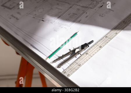 Metal ruler, compasses and green pencil are resting on blueprint on drafting table with shadow Stock Photo