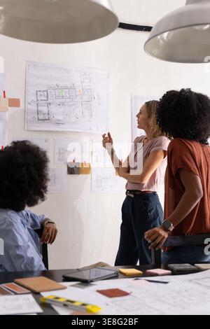 Diverse female coworkers pointing and reviewing architectural blueprints with swatches in studio Stock Photo