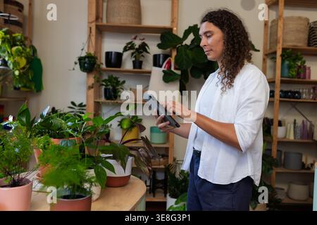 Non-binary person wearing white shirt, holding tablet, arranging pots on wooden table, copy space Stock Photo