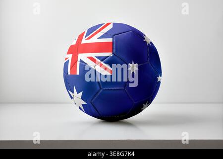A soccer ball printed with the Australian flag sits centered on a clean white surface with soft lighting and minimal shadows. Stock Photo