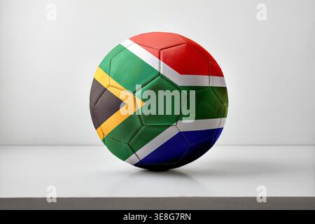 A soccer ball featuring the South African flag rests on a clean white surface with soft lighting, highlighting its colorful geometric pattern and stit Stock Photo