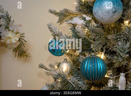 Close up of blue and white Christmas baubles and decorations on frosted tree branches with warm fairy lights, festive home interior scene Stock Photo