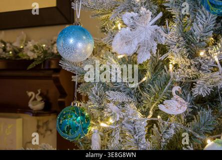 Close up of blue and white Christmas baubles and decorations on frosted tree branches with warm fairy lights, festive seasonal detail Stock Photo