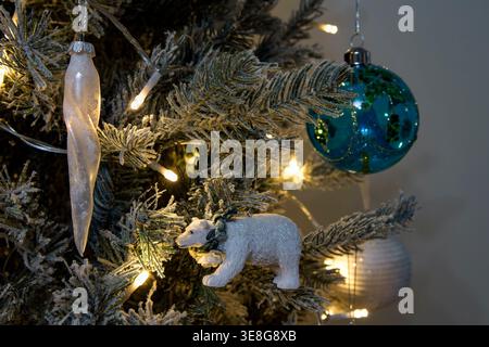 Close up of frosted Christmas tree with blue baubles, polar bear ornament and warm white lights in cosy indoor festive setting Stock Photo