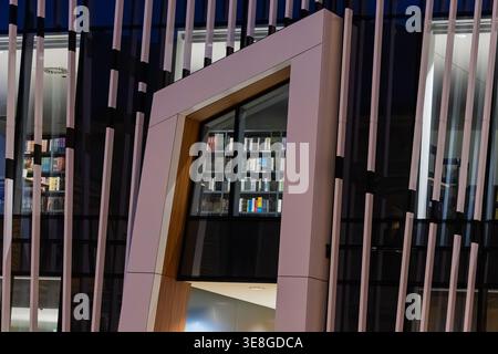 Vinkovci, Croatia - March 22.2026: A modern library interior visible through a geometric window frame in a contemporary urban building, showing illumi Stock Photo