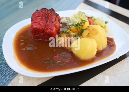 Overcooked stuffed red bell pepper with potatoes, lettuce, and plenty of brown sauce, traditional dish served on a plate at a casual dining restaurant Stock Photo