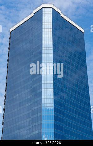 Modern Blue Glass Skyscraper Tower With Reflective Facade and Geometric Corner Against Cloudy Sky Stock Photo