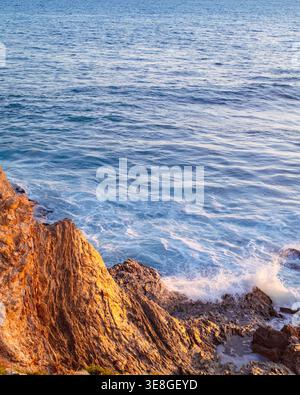 Waves crashing on rocks at beach at sunset Stock Photo