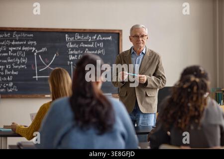 Portrait of Senior Man Teaching Economics to Students in Classroom Stock Photo