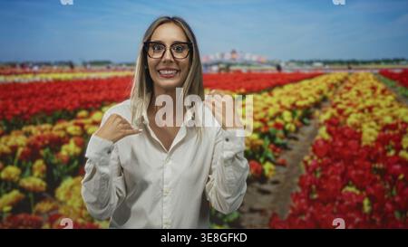 Woman smiling with hands slightly raised among tulip flowers in studio setting near colorful field; spring joy. Stock Photo
