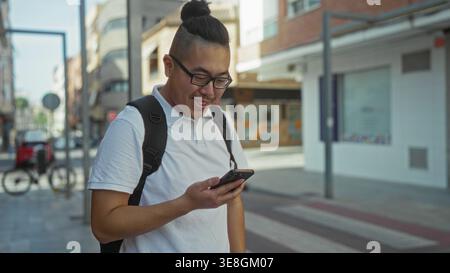 Man wearing glasses and white polo holding smartphone with visible hand and backpack on urban street beside storefront and bicycle rack, checking scre Stock Photo