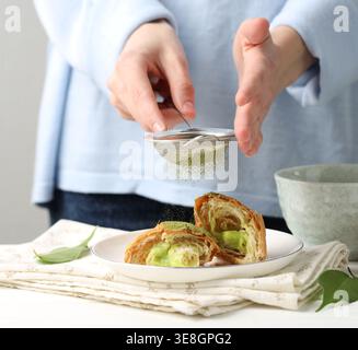 Woman sifting matcha powder onto croissant at white wooden table, closeup Stock Photo