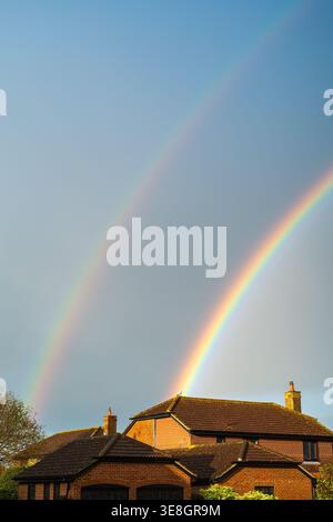 Double rainbow over the roof on a red brick house. A seagull is caught in the colours of the rainbow on the roof Stock Photo