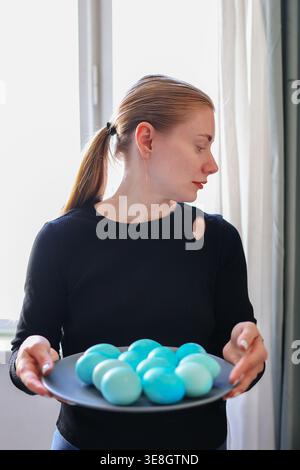 Female holding plate of blue eggs, joyful Easter preparation and seasonal lifestyle. Stock Photo