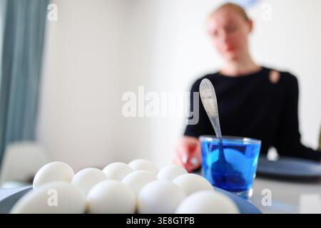 Home Easter preparation, dyeing eggs in blue liquid, simple festive lifestyle scene. Stock Photo