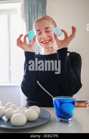 Woman holding blue Easter eggs over eyes, playful mood and festive spring celebration. Stock Photo